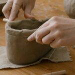 Close-up of hands shaping clay pottery with sculpting tools in a workshop.